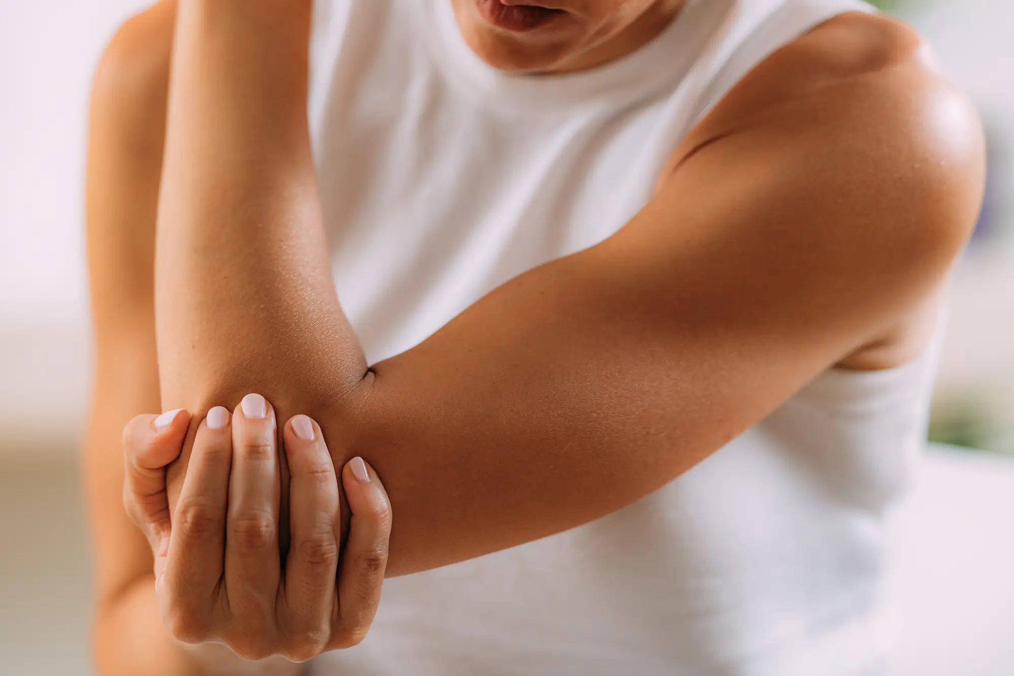 Person experiencing elbow pain while holding their arm, illustrating symptoms related to elbow, wrist, and hand discomfort in a physical therapy context.