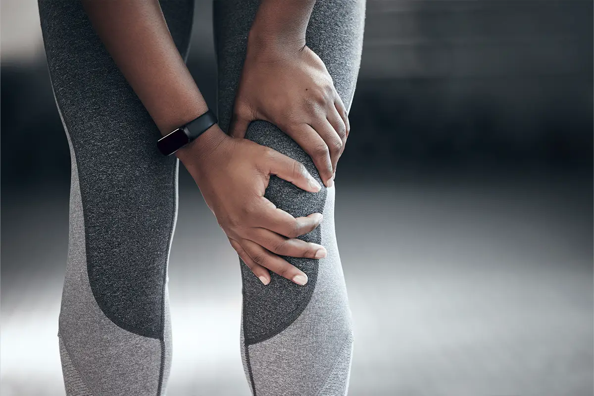 Person in athletic wear holding their knee, indicating knee pain, relevant to physical therapy and rehabilitation services.