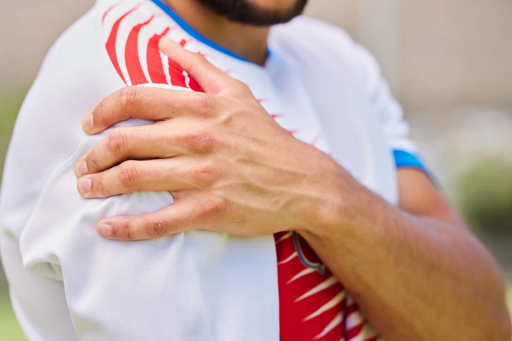 Man in sports jersey holding his shoulder, indicating discomfort related to joint pain, relevant to joint pain treatment in Tampa.